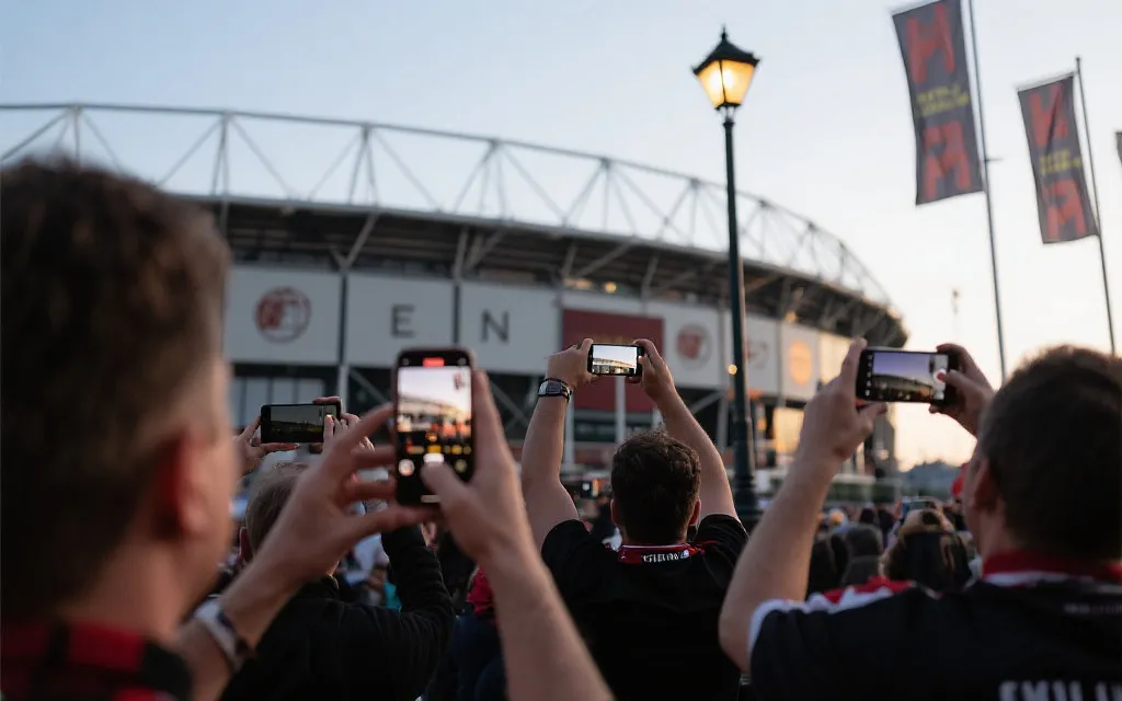 球场外球迷用手机拍摄短视频与合影，街头灯光与旗帜交织的纪实场景